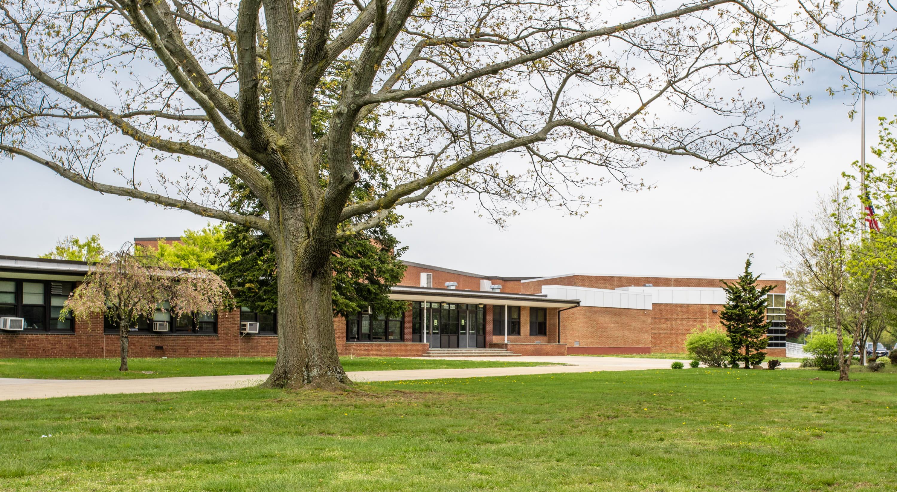 Security Systems for Schools Header Security systems for schools, demostrated by an exterior shot of one story brick school with tree in foregroun