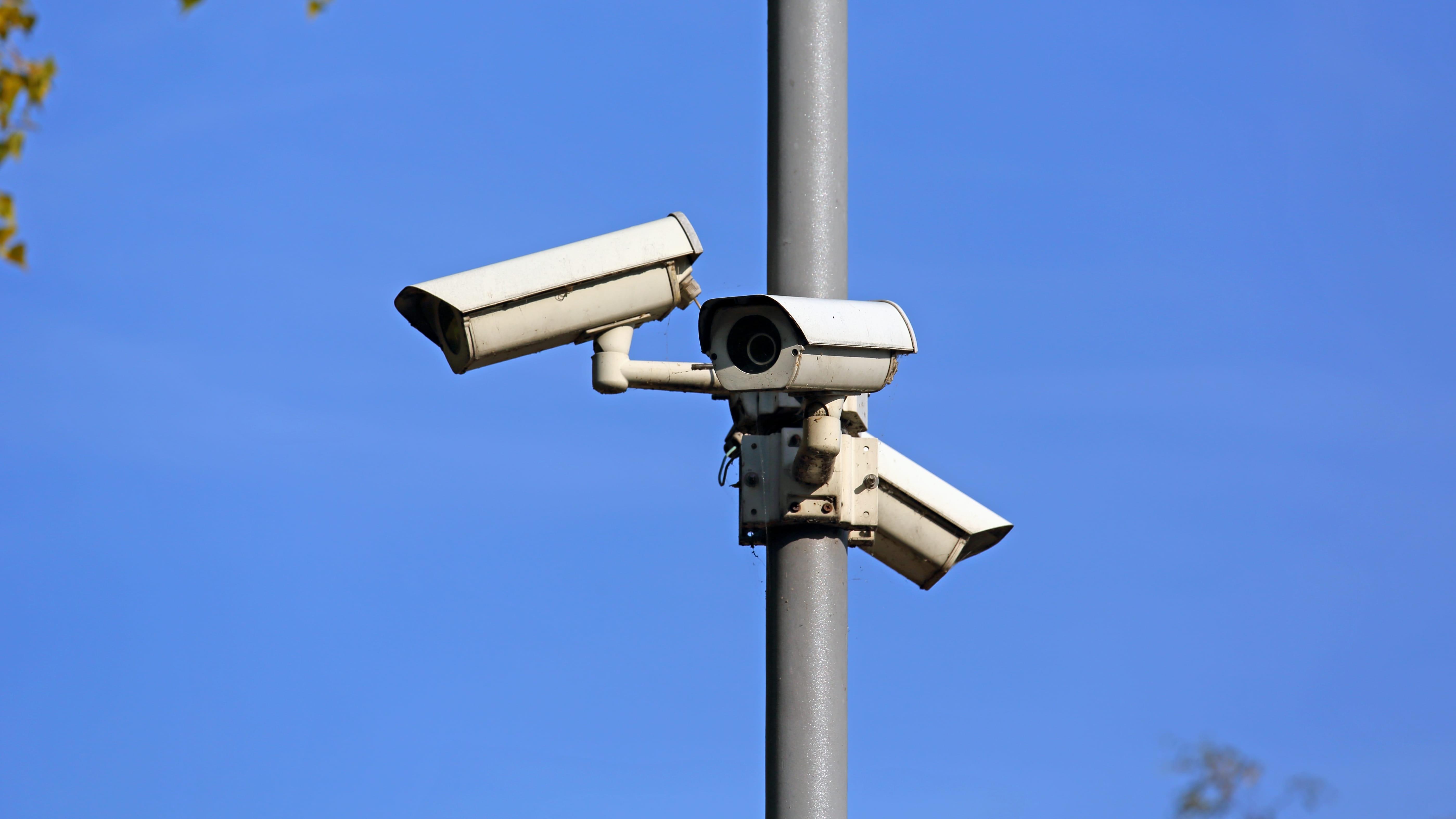 CCTV on white pole providing security systems for schools with brick building in background
