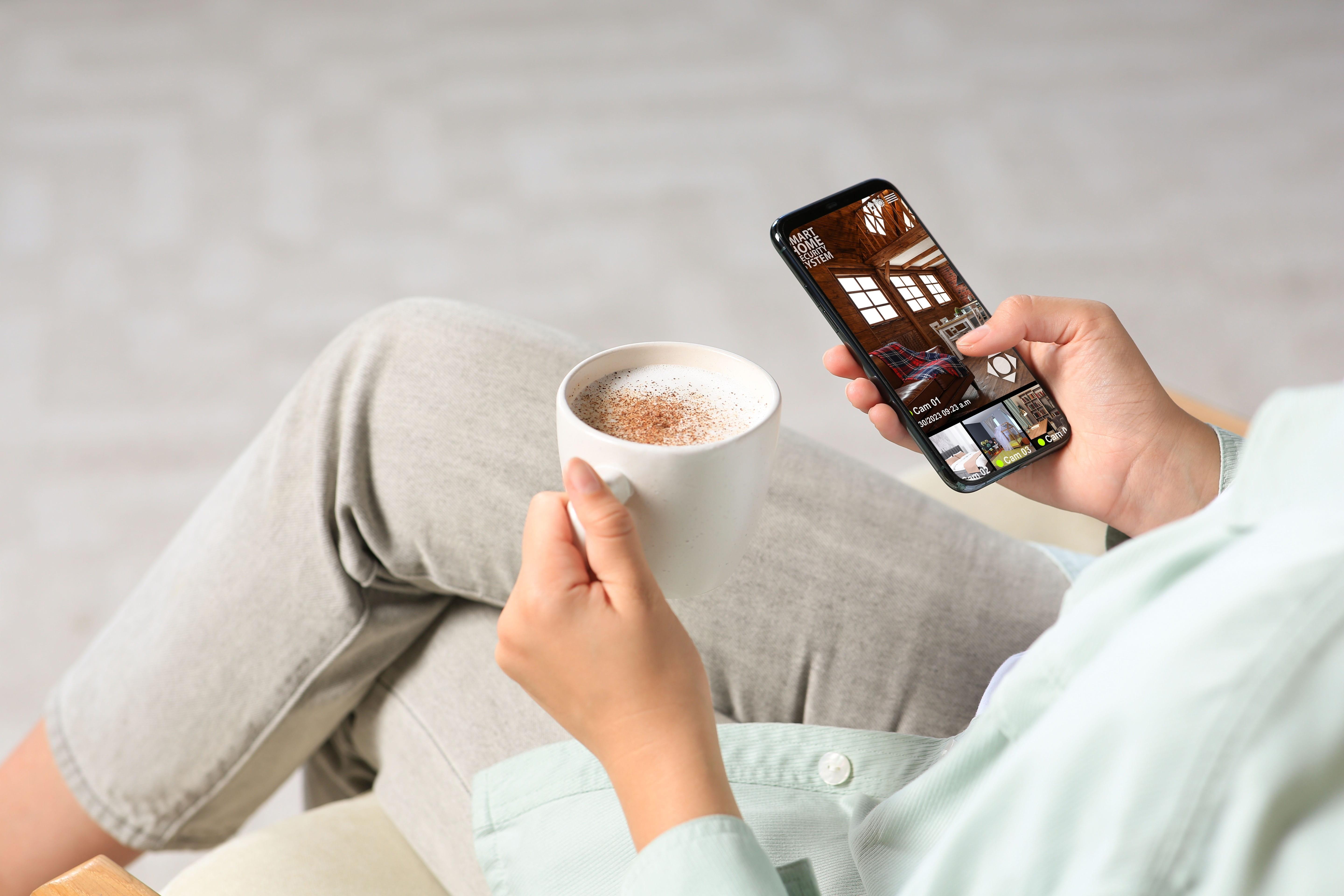 Remote Access CCTV Feature Woman drinking coffee while watching remote access CCTV on her smartphone